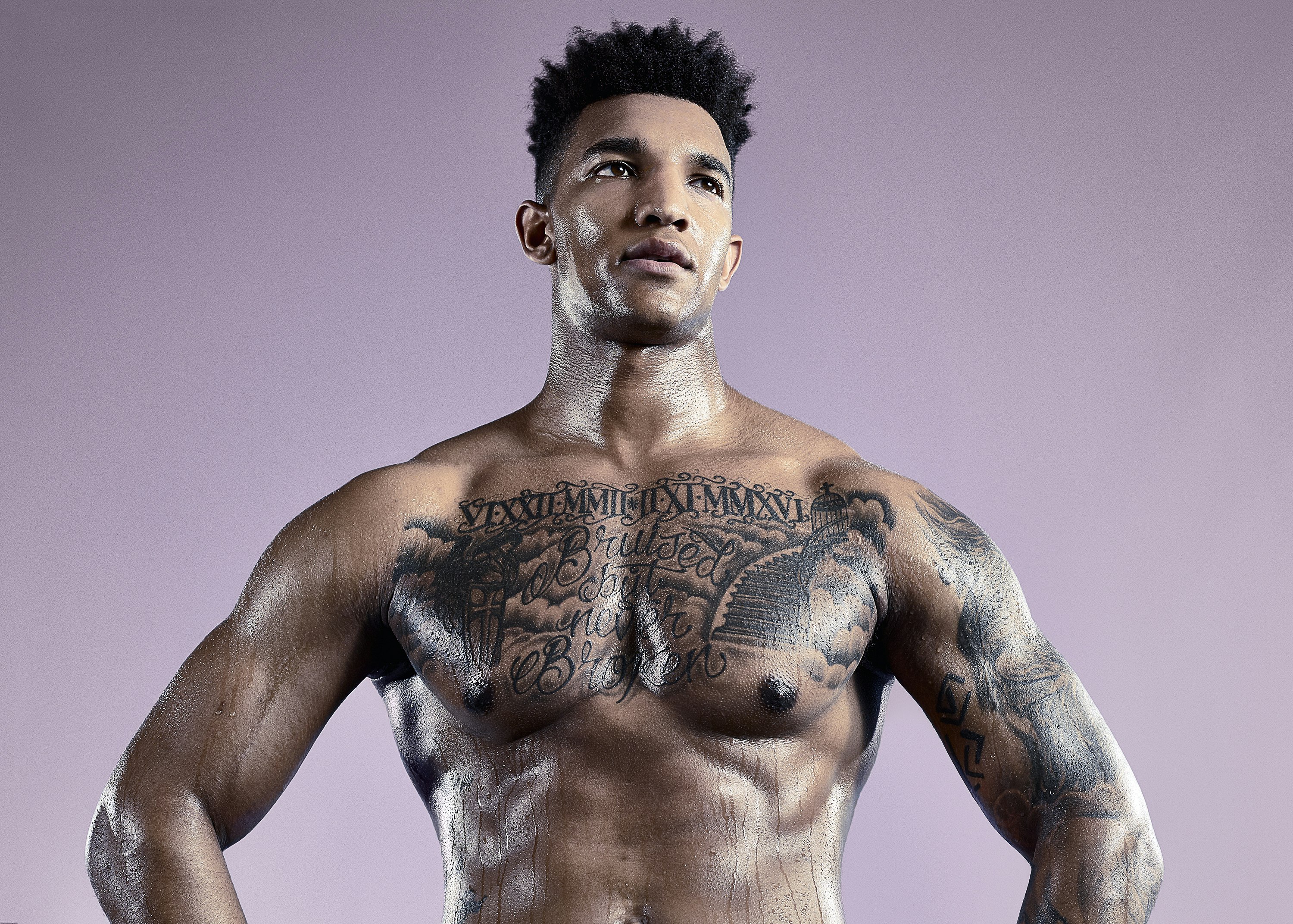 Athletic adult man with tattoos posing shirtless against a purple background in a studio environment, showcasing strength and fitness.