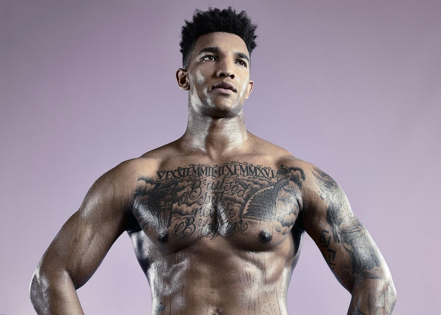 Athletic adult man with tattoos posing shirtless against a purple background in a studio environment, showcasing strength and fitness.