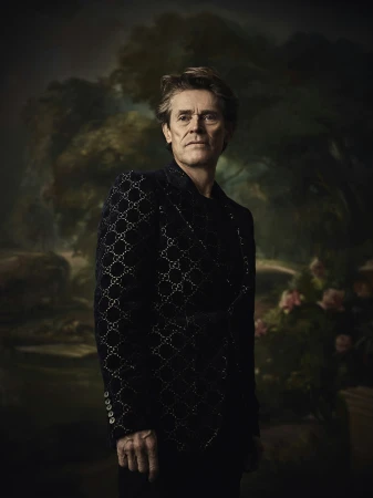 Portrait of older adult male in patterned jacket, posing indoors against a floral backdrop in a classic, formal style.