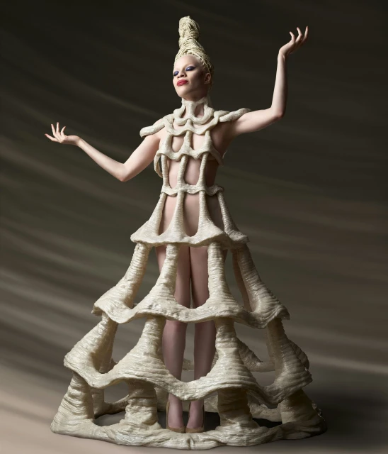 Albino model in unique sculptural dress posing in photo studio with outstretched arms and hands, dramatic lighting and earth-tone backdrop.