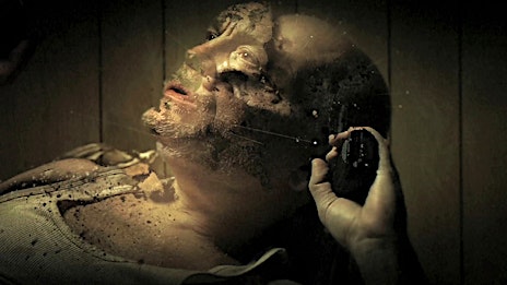 Disturbing close-up of an adult male's face with discoloration and an object in hand, set against a dimly lit, textured background.