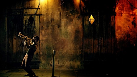 Night scene of a man playing the trumpet in an alleyway, illuminated by dim, yellow light and casting long shadows.