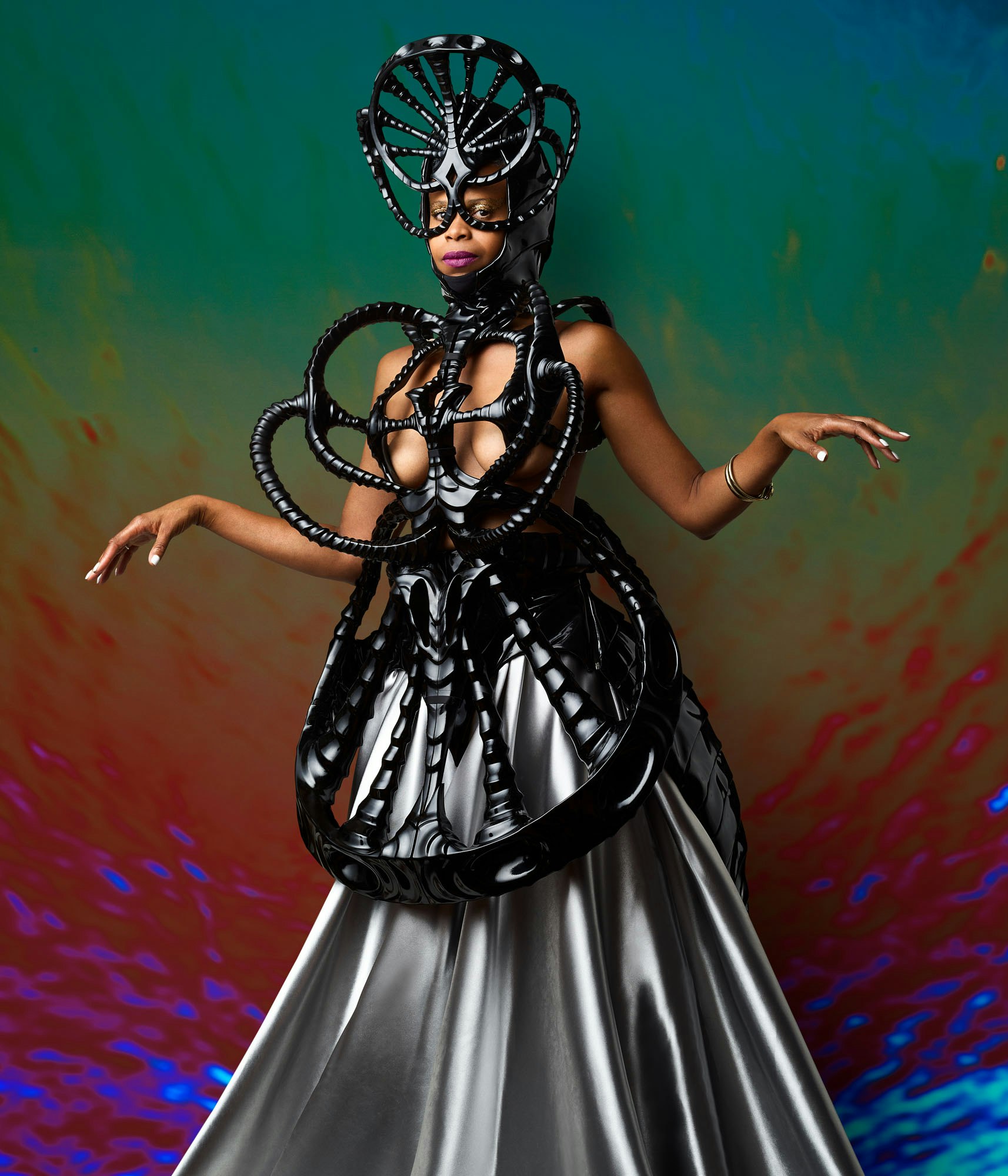 Woman posing in elaborate headpiece and dress with black structural design on a multi-color backdrop. Conceptual fashion.