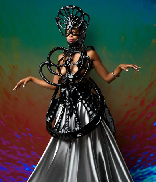 Woman posing in elaborate headpiece and dress with black structural design on a multi-color backdrop. Conceptual fashion.