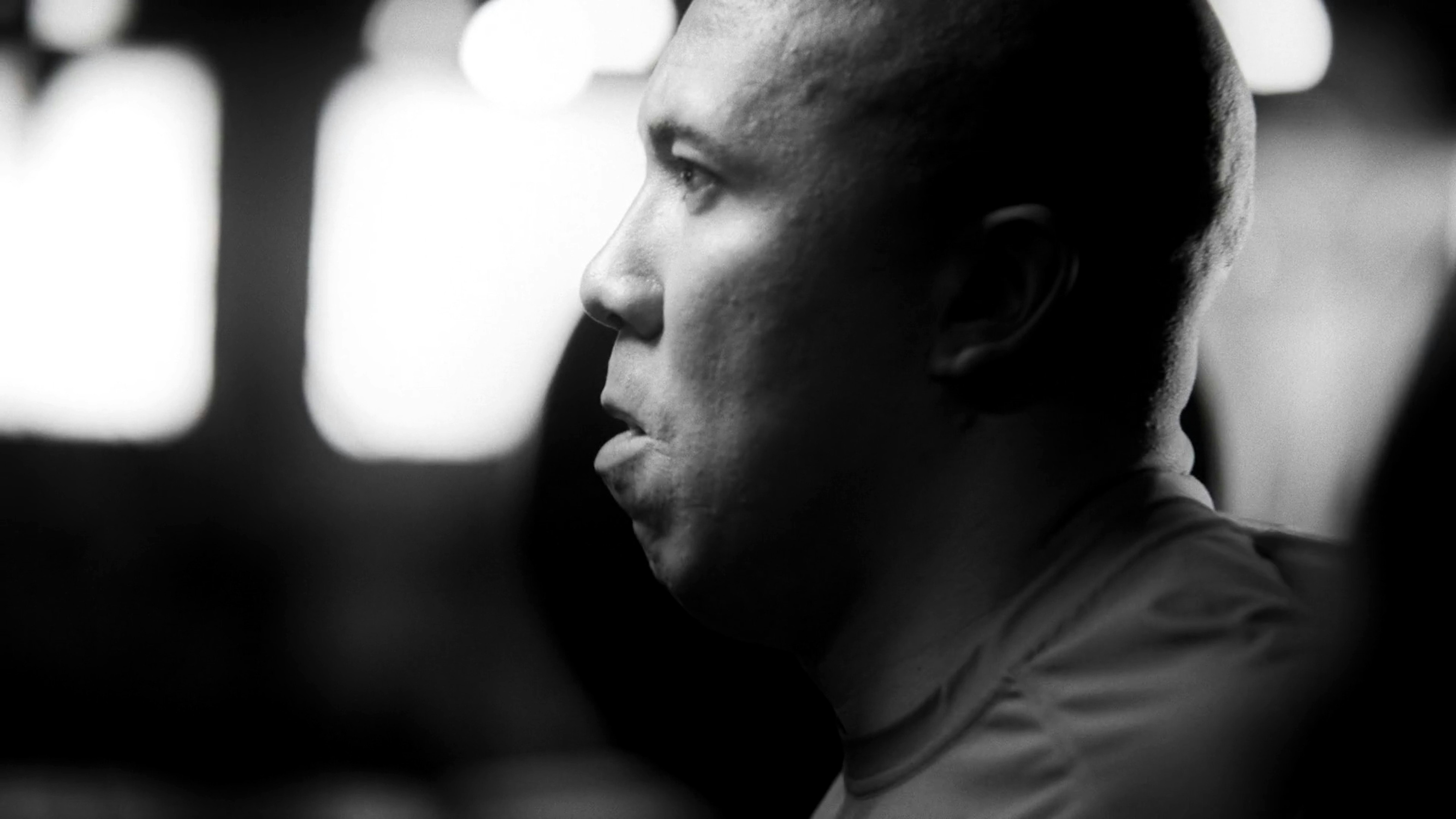 Monochrome portrait of a light-skinned adult male in a close-up profile with blurred lights in the background, focusing on facial details.