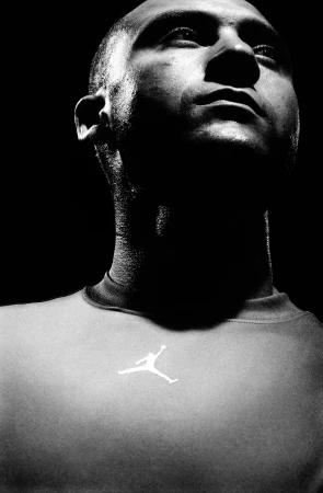 Low angle monochrome portrait of a bald man wearing an athletic t-shirt with a white jumping man logo in Chicago.
