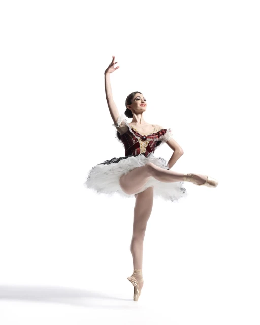 A ballerina in a red and white tutu, en pointe, dances against a white background, striking an elegant pose with arm raised.