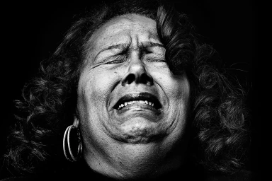 Close-up monochrome portrait of an older woman with an intense emotional expression against a dark background