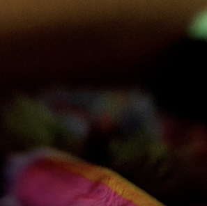 Blurred close-up of brightly colored fabrics in shades of pink, yellow, green and brown.