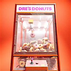 A vintage claw machine filled with donuts, illuminated against a vibrant orange background, featuring the text 'DRE'S DONUTS' on top.