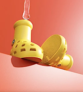 Eye-level studio shot of two yellow Croc rain boots sitting on an orange surface with water pouring into the boot on the left.