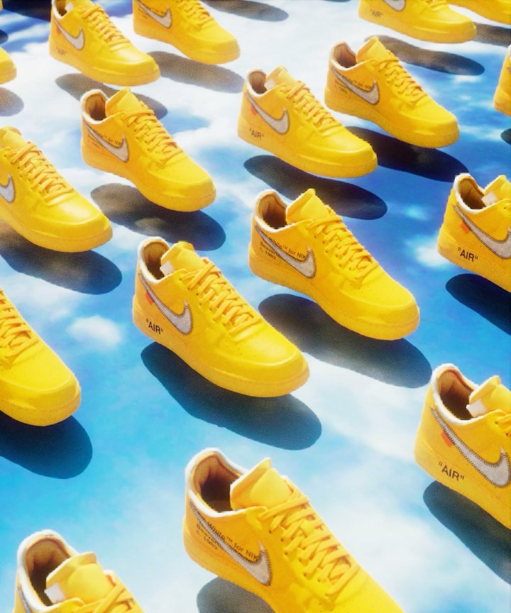 Numerous yellow Nike Air Force 1 sneakers with white swooshes create a dynamic grid pattern against a cloudy sky backdrop.