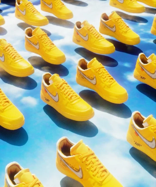 Numerous yellow Nike Air Force 1 sneakers with white swooshes create a dynamic grid pattern against a cloudy sky backdrop.