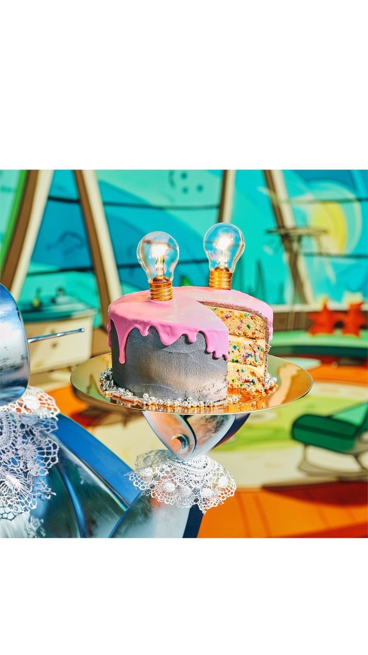 Whimsical cake decorated with lightbulbs on a silver platter, against a colorful cartoon-style background. Perfect for creative celebrations.