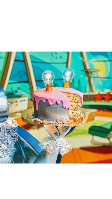 Whimsical cake decorated with lightbulbs on a silver platter, against a colorful cartoon-style background. Perfect for creative celebrations.