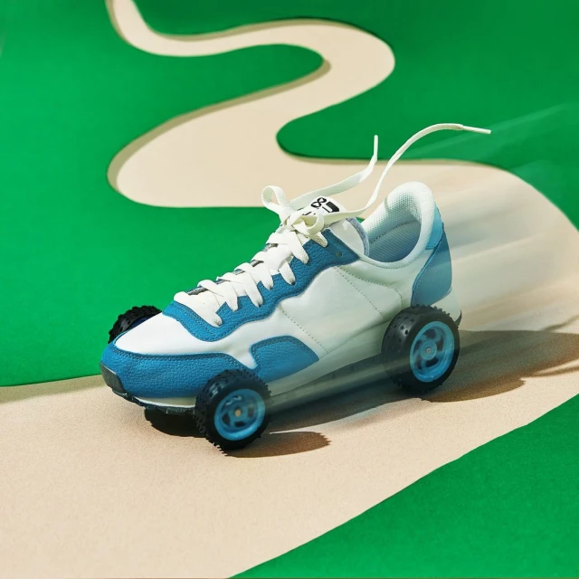 White and blue sneaker with toy wheels pictured on a green and tan background resembling a race track, studio shot.