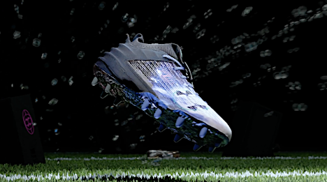 Digitally rendered football cleat in mid-air against a dark background with simulated lights on artificial turf with black box prop.