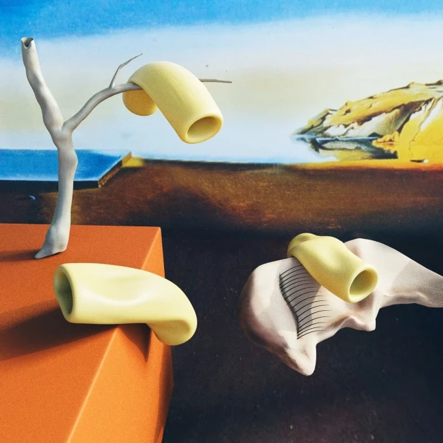 Surreal art featuring yellow forms on platform and tree branch against an abstract landscape backdrop with blue sky and brown land.