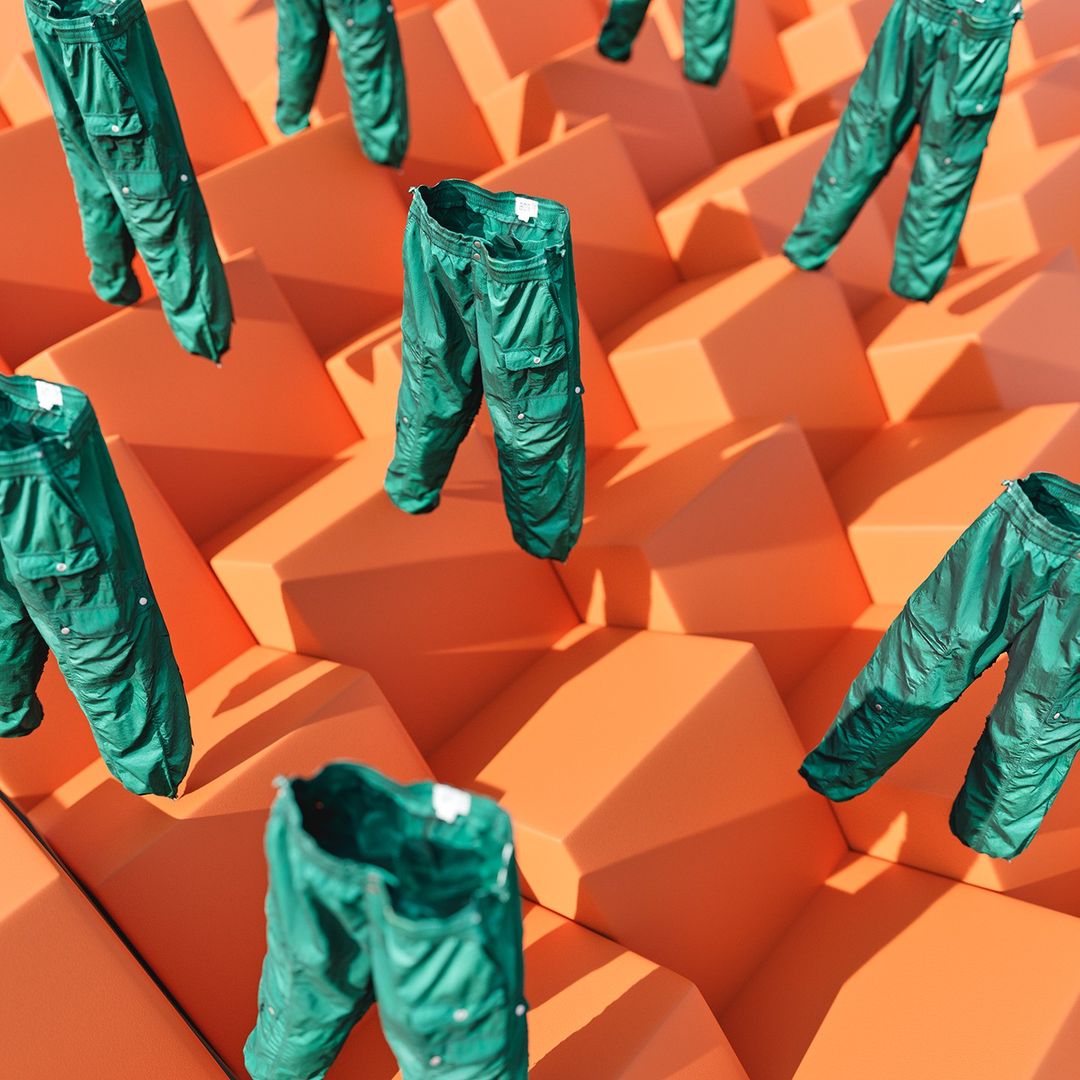 Several pairs of green cargo pants are floating in a grid pattern over a geometrically textured orange block background.