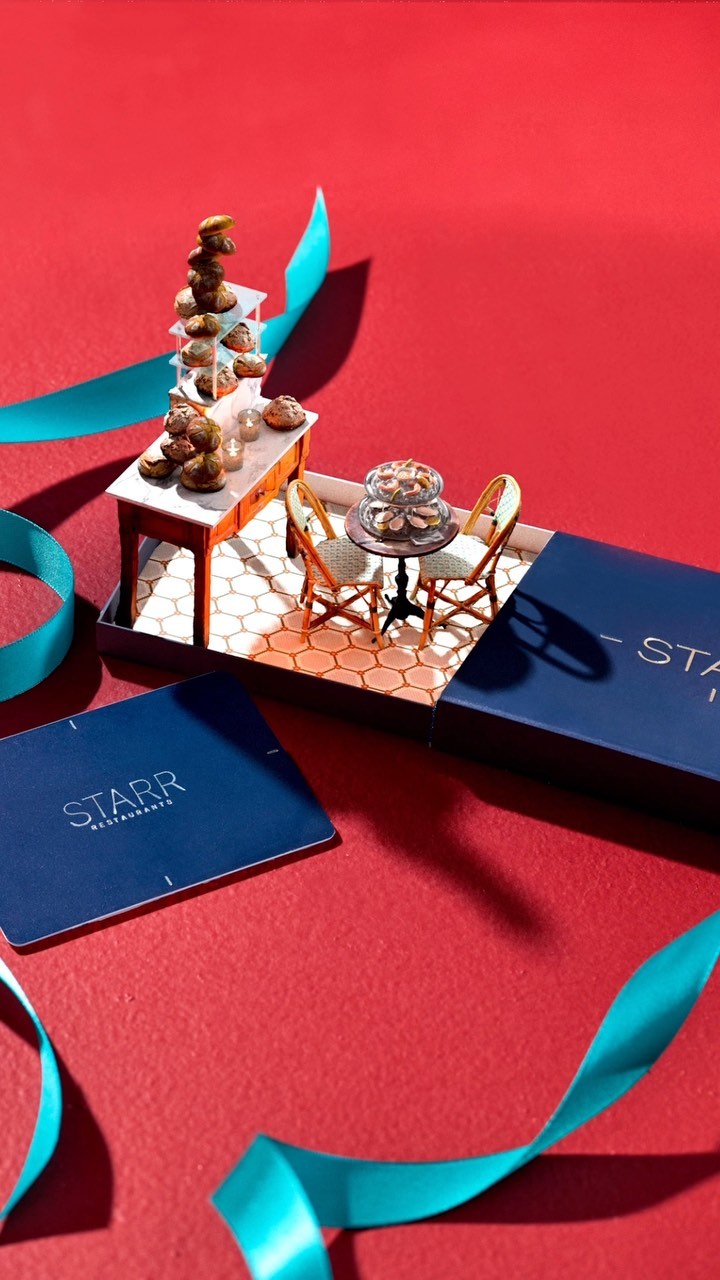 Small table and chairs are decorated with mini donuts, with blue ribbons and a gift card on a vibrant red background.