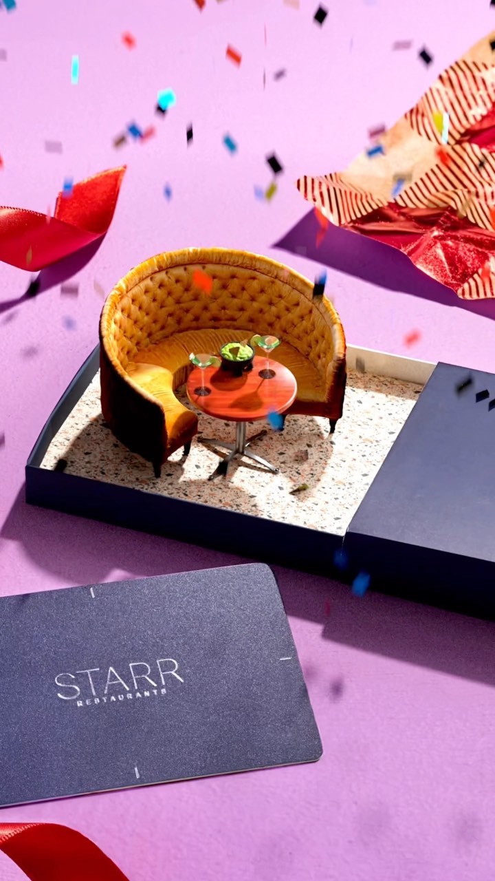 A small-scale scene featuring a miniature seating area with table and chairs set on a flat surface, confetti, and a brand card.