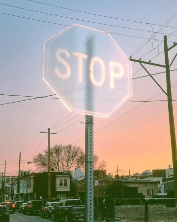 Urban street scene at dusk with a prominent stop sign, parked cars, and row houses under a pastel gradient sky.