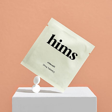 Package of hims sildenafil erectile dysfunction medicine balanced on a white block with two tablets against a peach colored background.