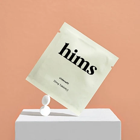 Package of hims sildenafil erectile dysfunction medicine balanced on a white block with two tablets against a peach colored background.