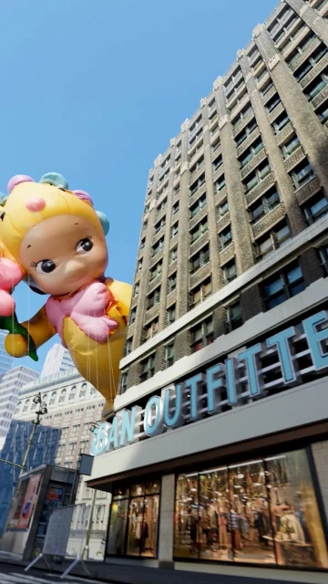Low-angle shot of a parade balloon in the shape of a cartoon character in front of a building on a sunny day in a city.