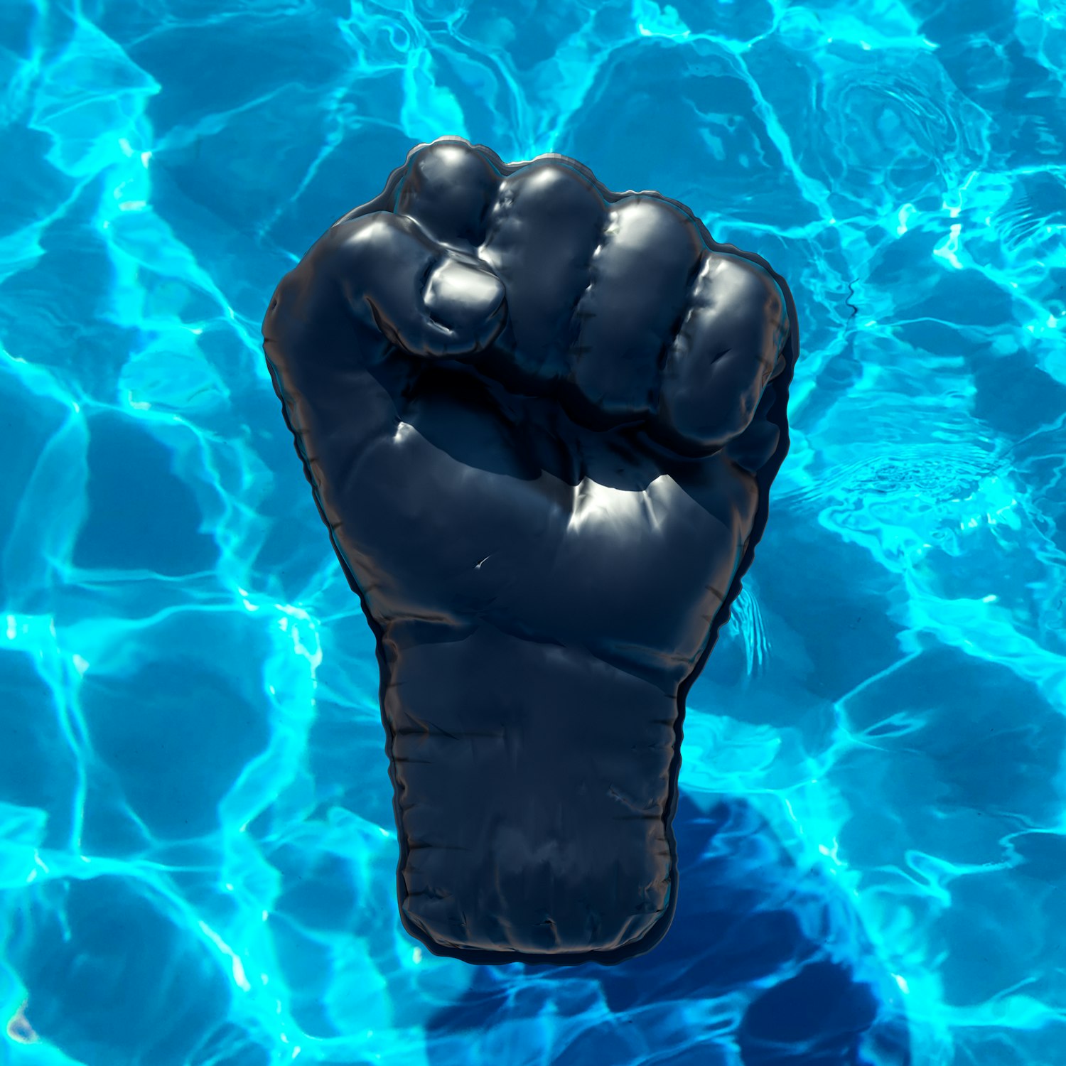 Inflatable black fist floats on the surface of a pool with clear blue water, creating rippling reflections and abstract patterns.