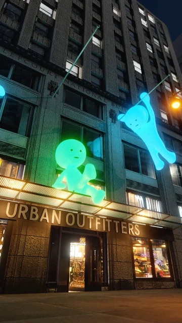 Exterior shot of the Urban Outfitters store, featuring animated figures on the facade, enhancing its urban setting at night.
