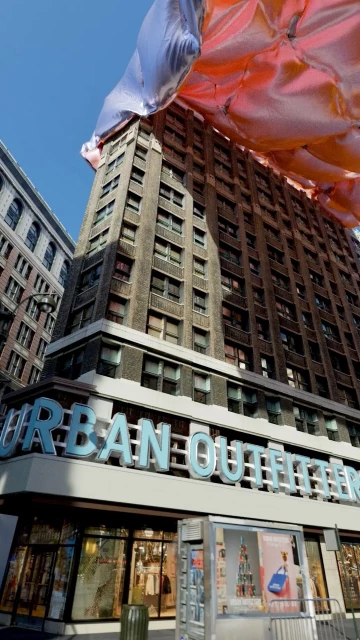 View of tall buildings, including an Urban Outfitters retail store, under a mostly clear blue sky, captured with a low-angle perspective.