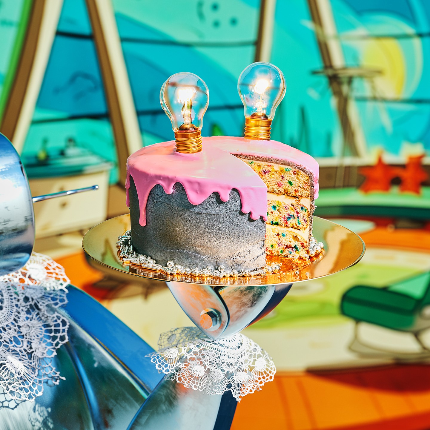 A festive grey and pink cake with lightbulbs on a gold platter stands against a colorful cartoon background, creating a playful vibe.