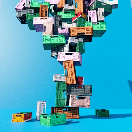 Stack of colorful plastic crates balanced on a blue background, creating a whimsical and playful visual composition.
