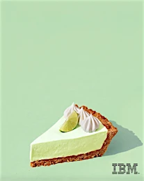Studio shot of a slice of key lime pie on a mint-green background, garnished with lime and meringue; IBM logo in corner.