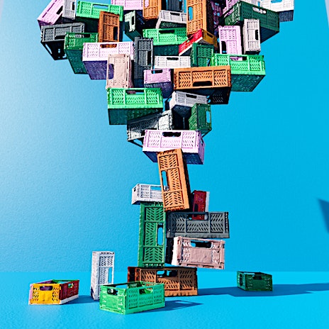 Stacked colorful plastic crates against a bright blue background create an abstract tower for storage and shipping, modern design.