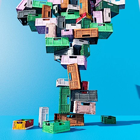 Stacked colorful plastic crates against a bright blue background create an abstract tower for storage and shipping, modern design.