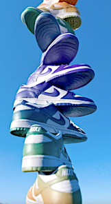 Stacked Nike Dunk sneakers in green, purple, and tan colors against a clear blue sky create an eye-catching vertical composition.