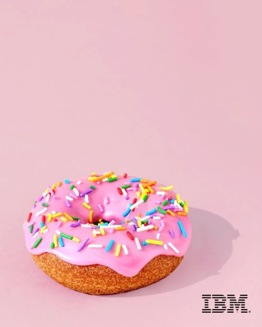 Eye-level studio shot of a pink donut with colorful sprinkles on a light pink backdrop with the IBM logo in the bottom right corner.