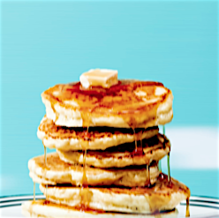 Stack of golden pancakes topped with melting butter and drizzled with syrup against a bright aqua background in a food photography shot.