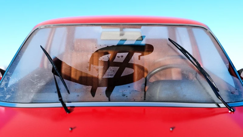 Red compact car with dollar sign drawn on the windshield and windshield wipers visible against a blue sky backdrop, close-up shot.