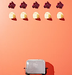 Top-down shot of a toaster with toast and topping on a peach background featuring a grid pattern and clean, bright studio lighting.