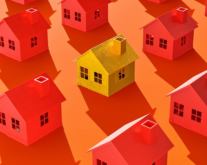 Aerial view of a collection of identical red toy houses with a single yellow house centered in the grouping on orange backdrop.