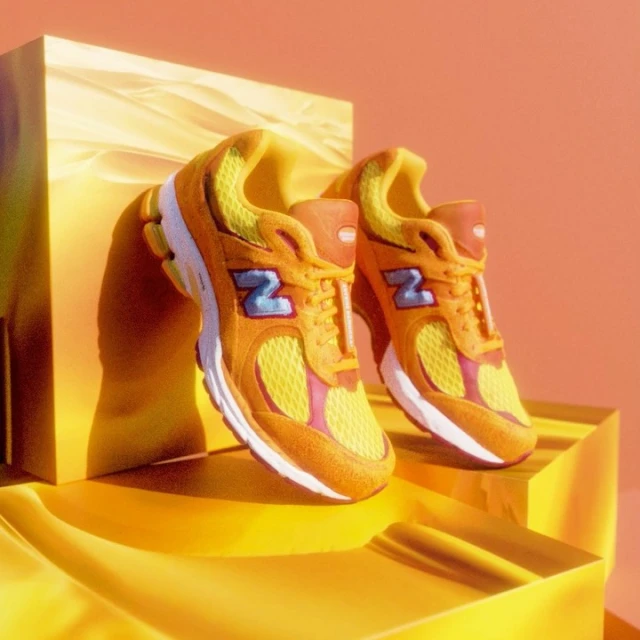 Studio shot of yellow and orange New Balance 2002R sneakers against a yellow geometric platform and a matching color gradient background.