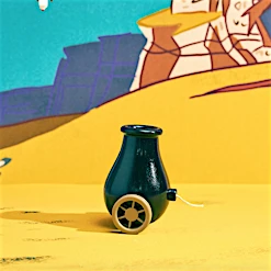Close-up studio shot of a toy cannon with wheels on a yellow surface against a cartoon desert backdrop, featuring mountains and blue sky.