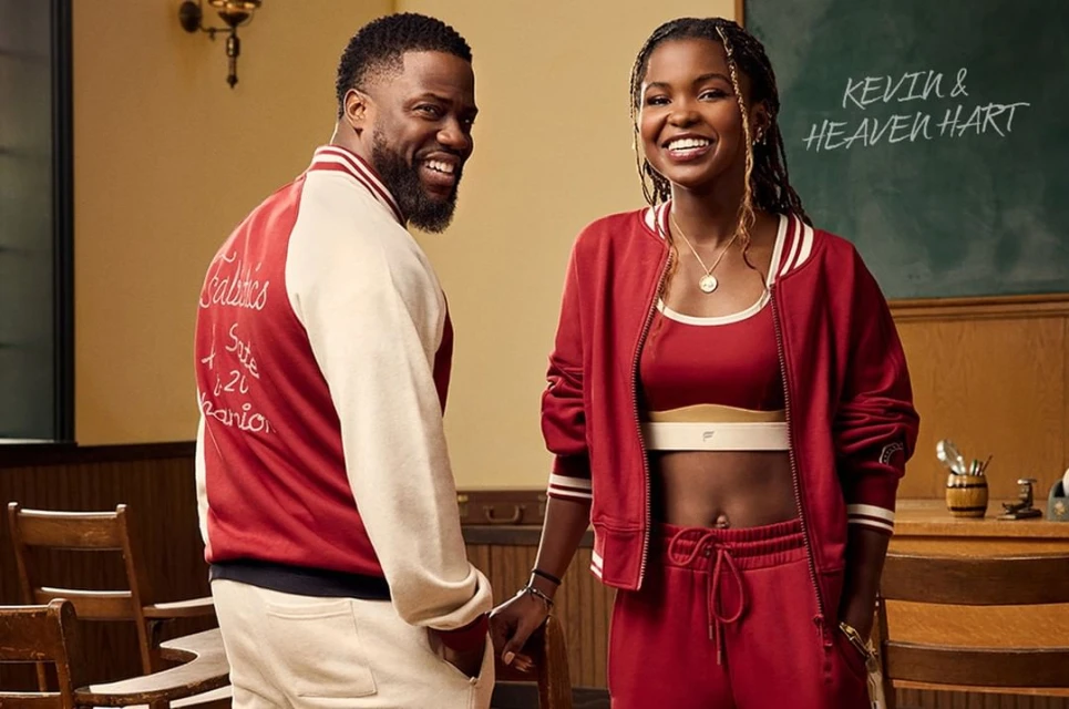 Kevin and Heaven Hart pose in a classroom setting wearing matching red outfits. Kevin wears a letterman jacket; Heaven wears a track suit.
