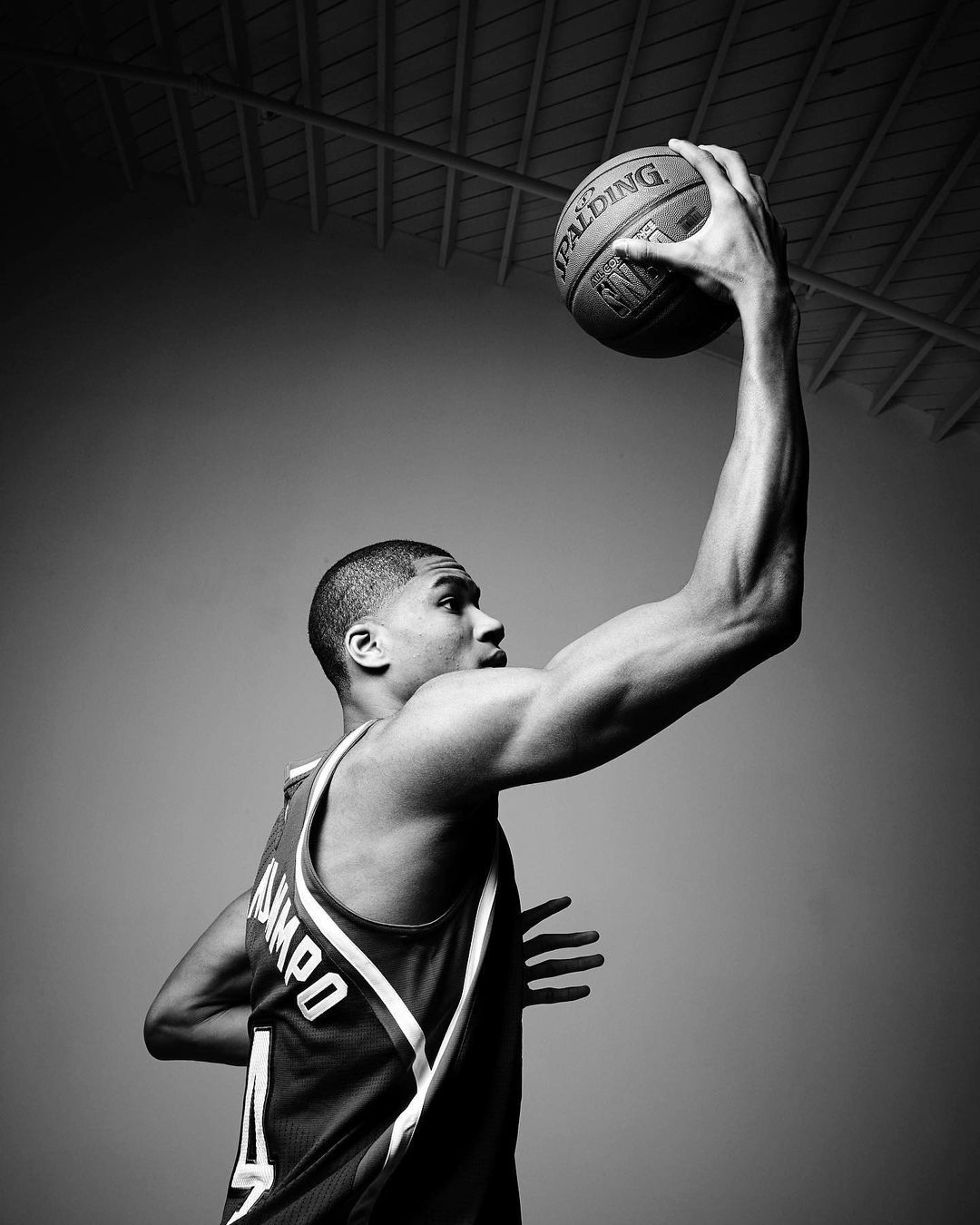 Black and white portrait of a muscular basketball player in uniform holding a Spalding NBA basketball, looking left, studio lighting.