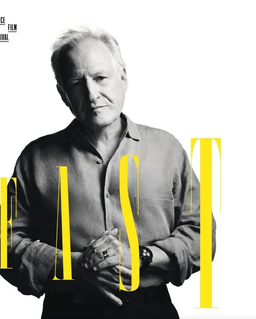 Promotional portrait of an adult male with silver hair, wearing a gray button-down shirt. Text is partially visible over the image.