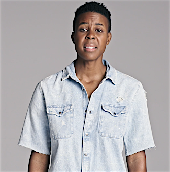 Close-up of an adult Black woman with short hair wearing a denim shirt in a photo studio with neutral grey background and diffused lighting.