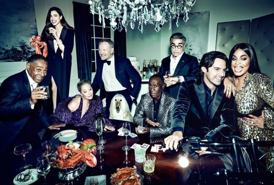 Group of celebrities in formal wear around a table laden with seafood, with a dog and motorcycle, posing for a portrait in a luxurious setting.